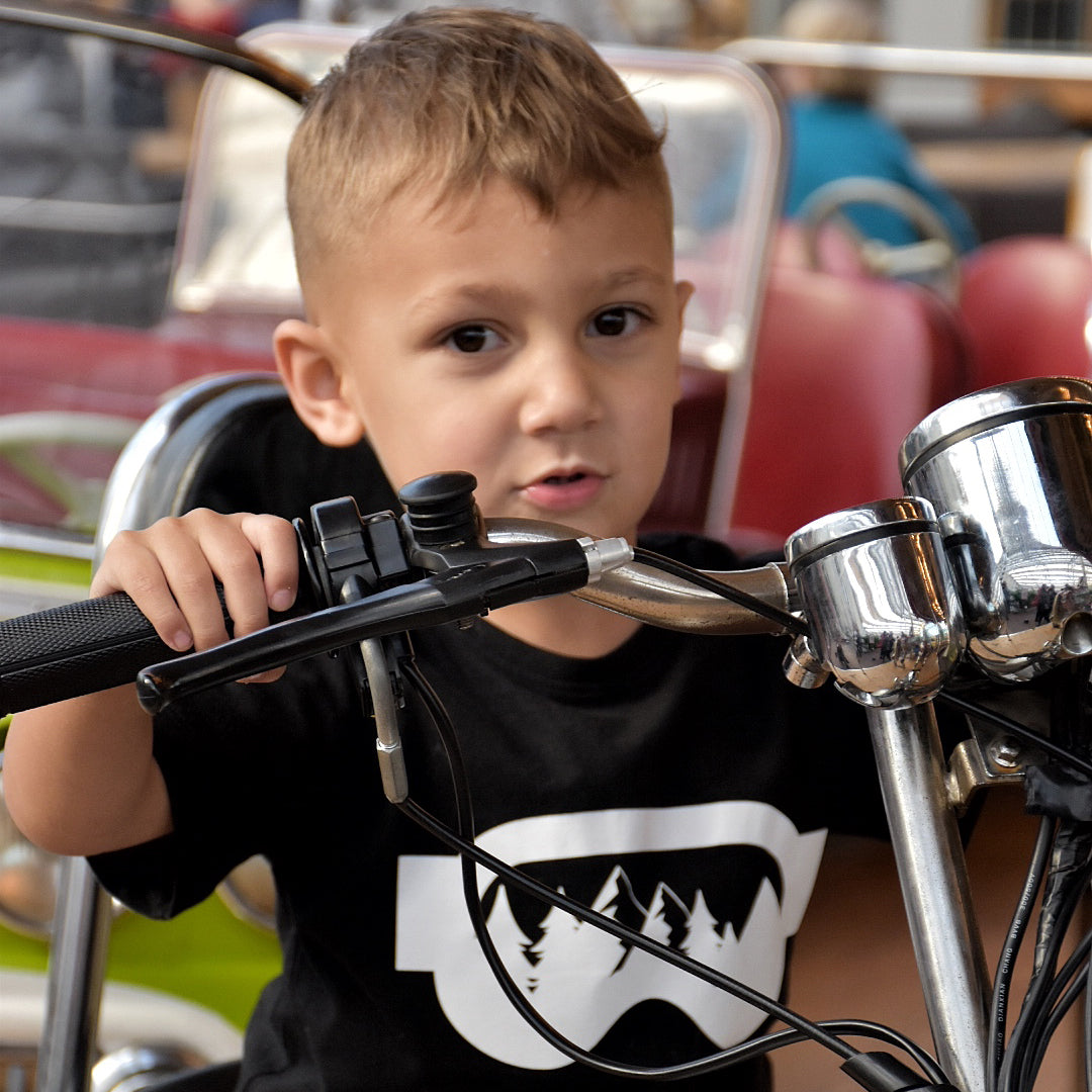 Young boy wearing black shirt with ski goggles print by KMLeon on motorcycle.