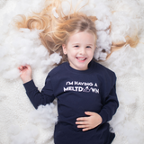 Smiling blonde girl laying on snow with hair spread out, wearing navy shirt with 'I'm having a meltdown' print by KMLeon.
