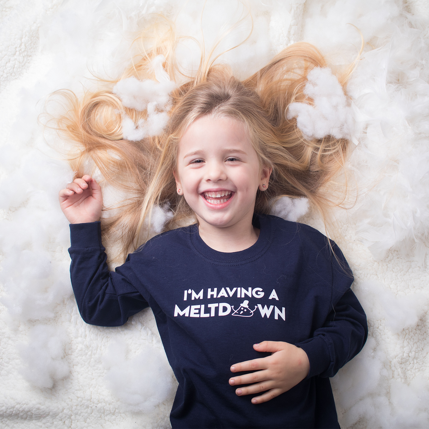 Laughing blonde girl laying on snow with hair spread out, wearing navy shirt with 'I'm having a meltdown' print by KMLeon.