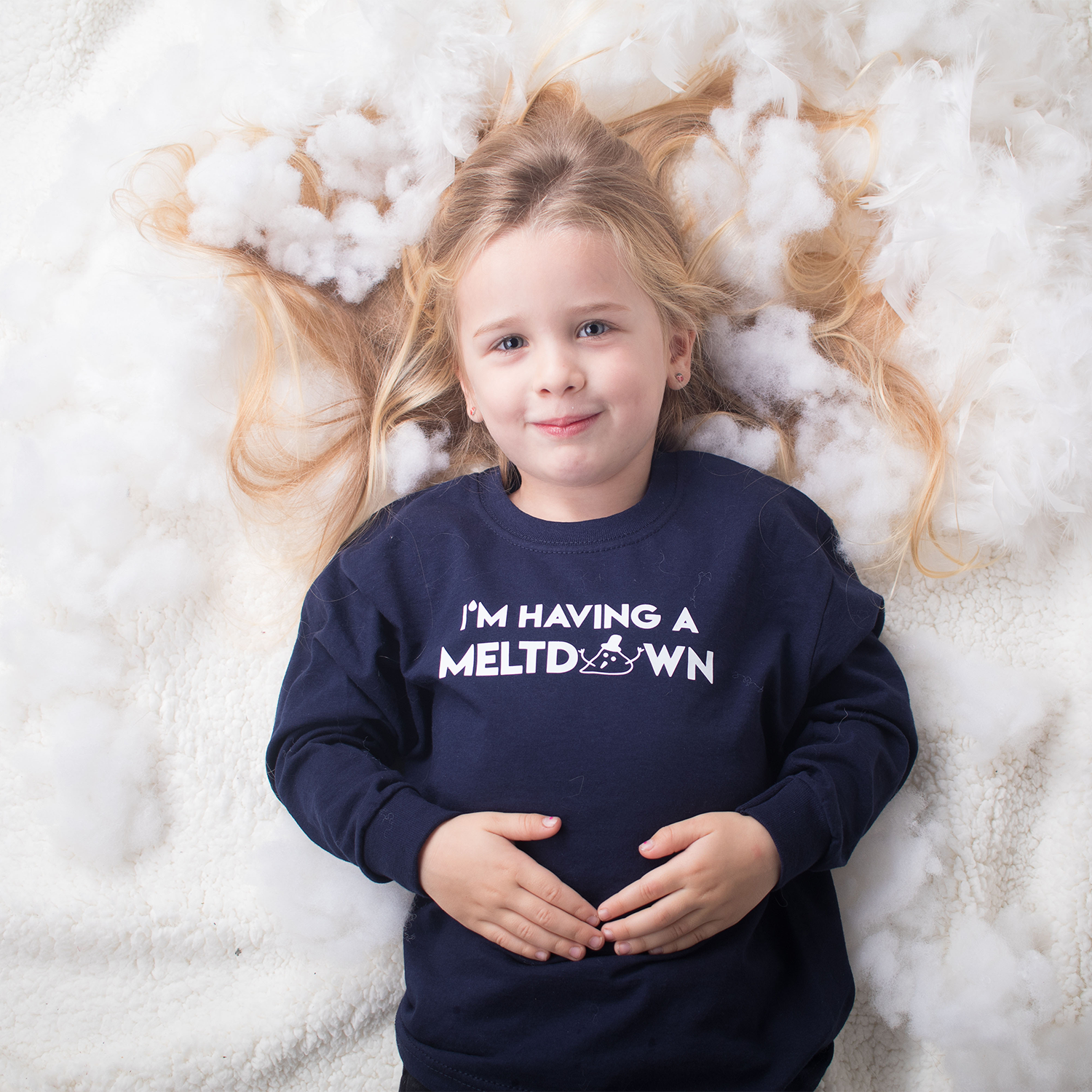 Blonde girl laying on snow with hair spread out, wearing navy shirt with 'I'm having a meltdown' print by KMLeon.