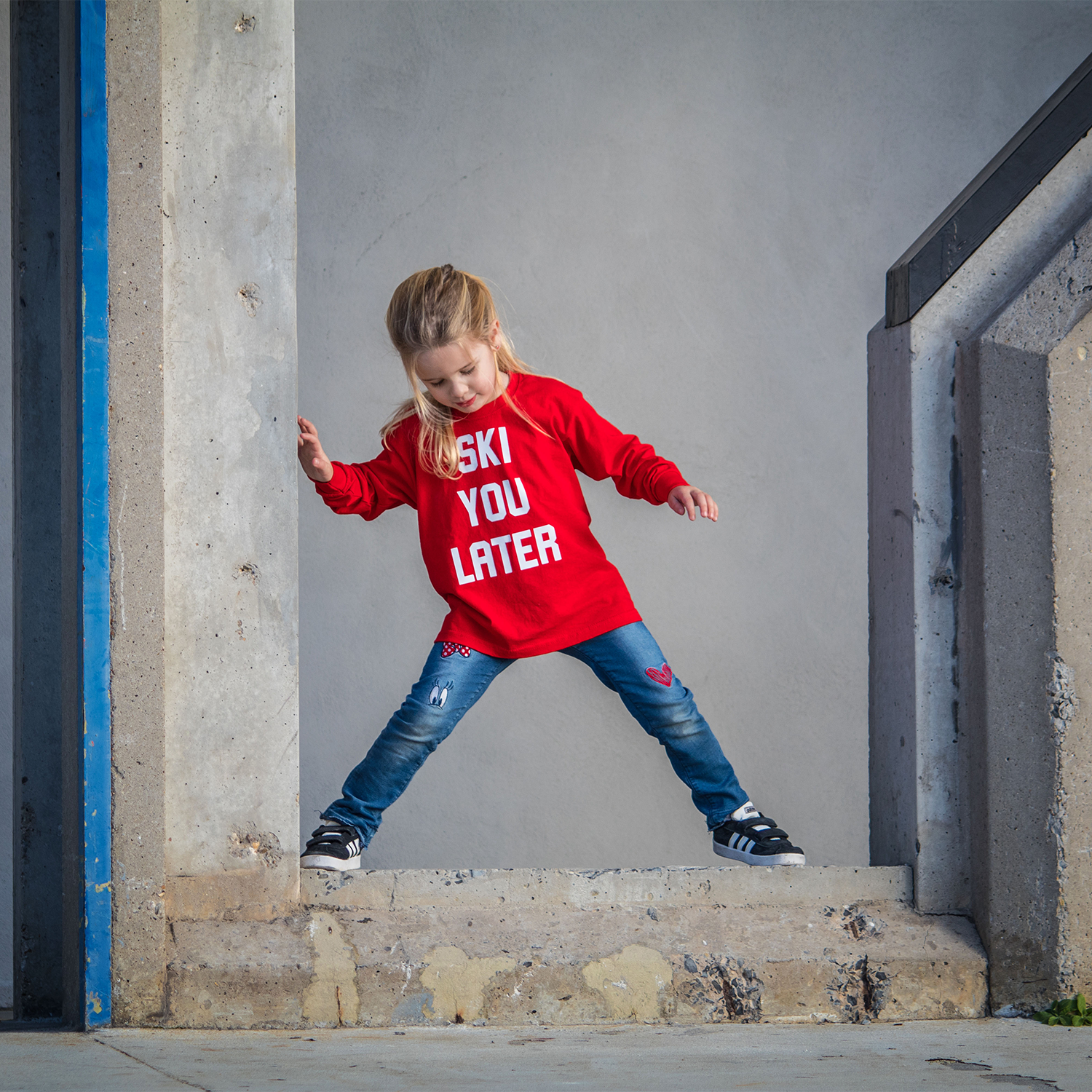 Blonde girl with red shirt with 'Ski je later' print by KMLeon standing on concrete.