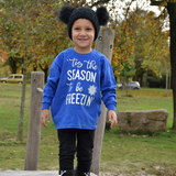 Boy in nature wearing black hat with pompoms and blue shirt with long sleeves with ''tis the season to be freezin'' print by KMLeon.