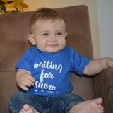 Smiling little boy in front of christmas tree, wearing blue shirt with 'Waiting for snow' print by KMLeon.