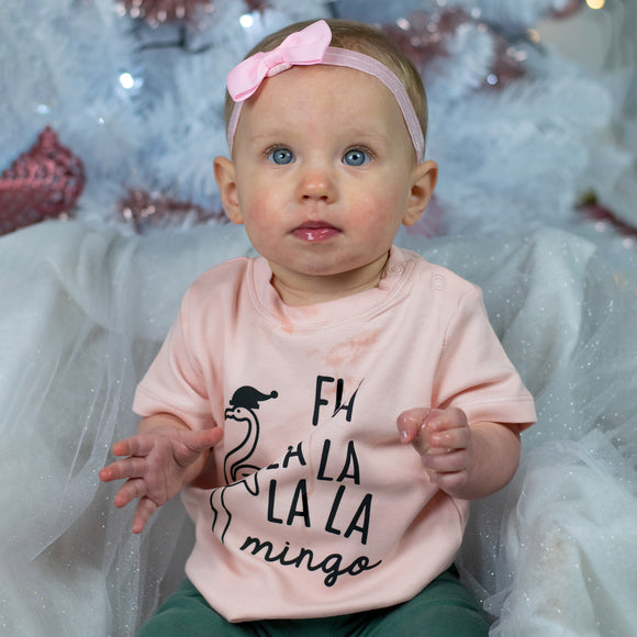 Baby girl with blue eyes, wearing a ppink headband and pink shirt, with 'Fla la la la la mingo' print by KMLeon looking up.