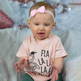 Baby girl with blue eyes, wearing a ppink headband and pink shirt, with 'Fla la la la la mingo' print by KMLeon looking down.
