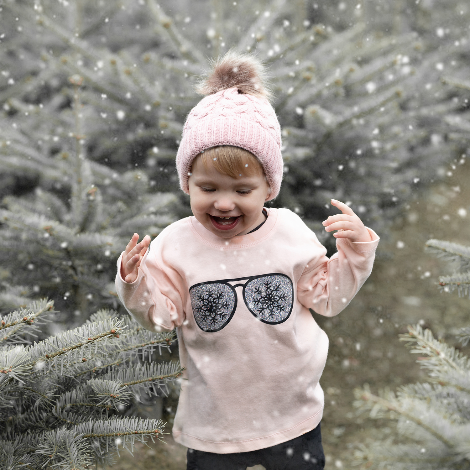 Happy blonde girl with pink beanie wearing pink shirt with long sleeves with glitter snow flake glasses print by KMLeon, laughing.