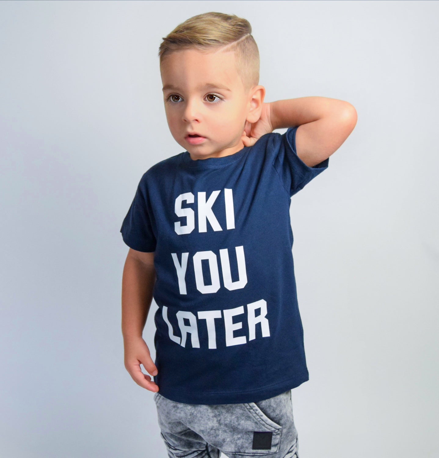 Boy wearing navy shirt with 'Ski je later' print by KMLeon, with hand in neck.