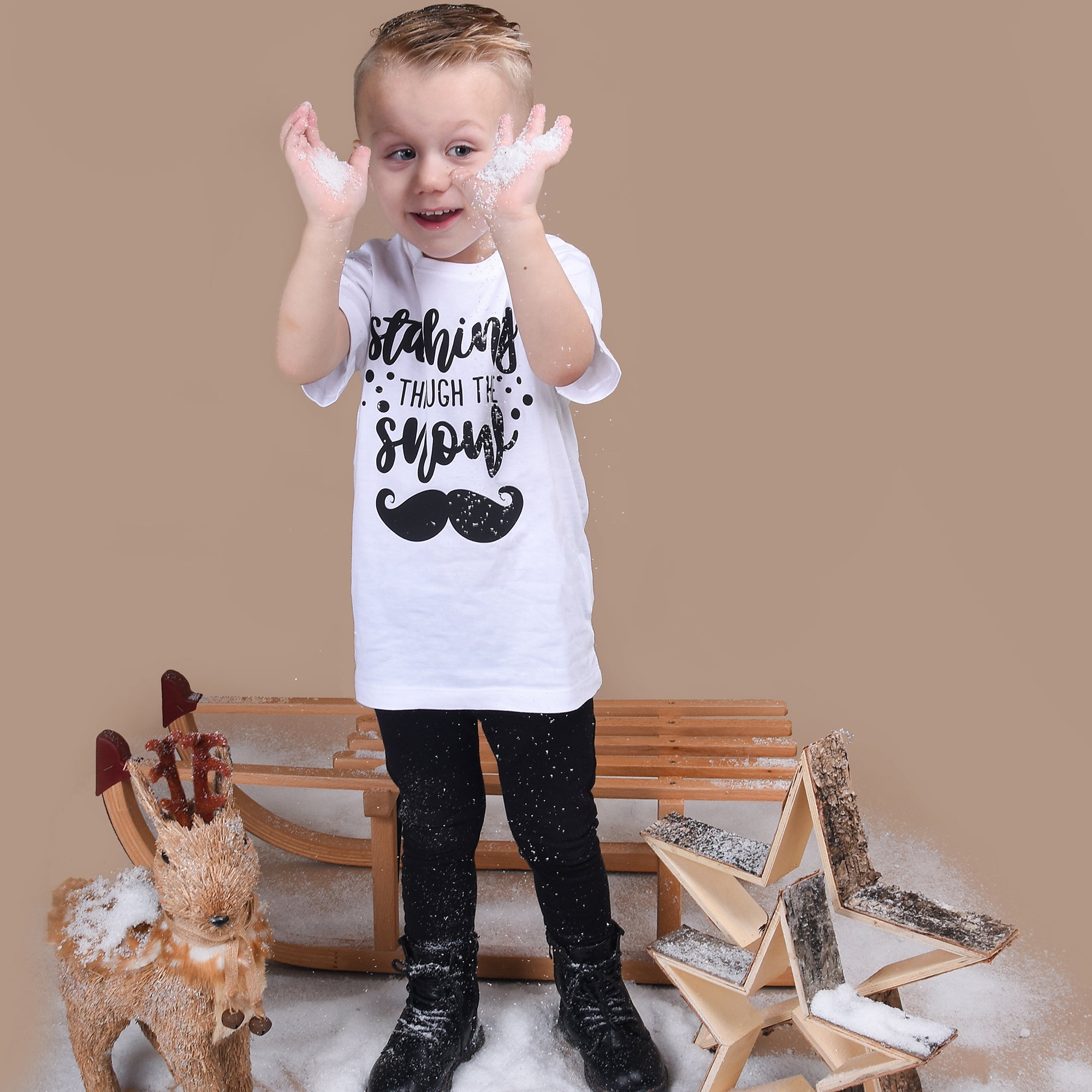 Blonde boy playing with snow, wearing white shirt with 'Staching through the snow' print by KMLeon.