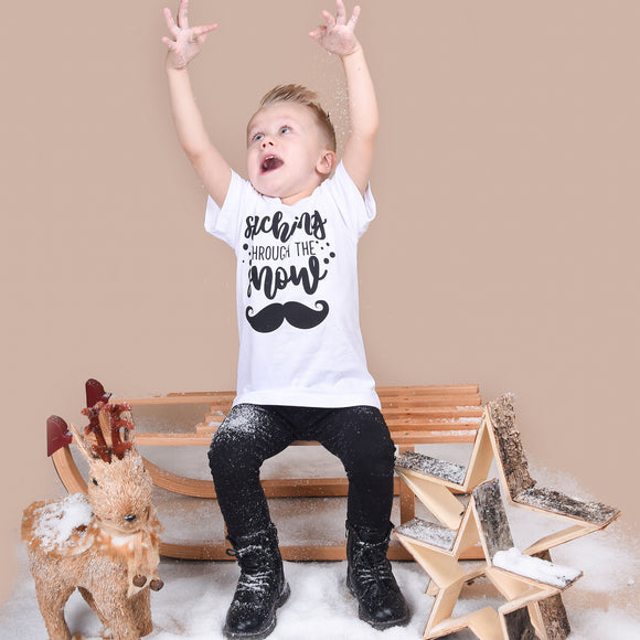 Blonde boy playing with snow, wearing white shirt with 'Staching through the snow' print by KMLeon.