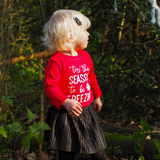 Blonde girl in forest wearing black skirt and red shirt with long sleeves with ''tis the season to be freezin'' print by KMLeon.