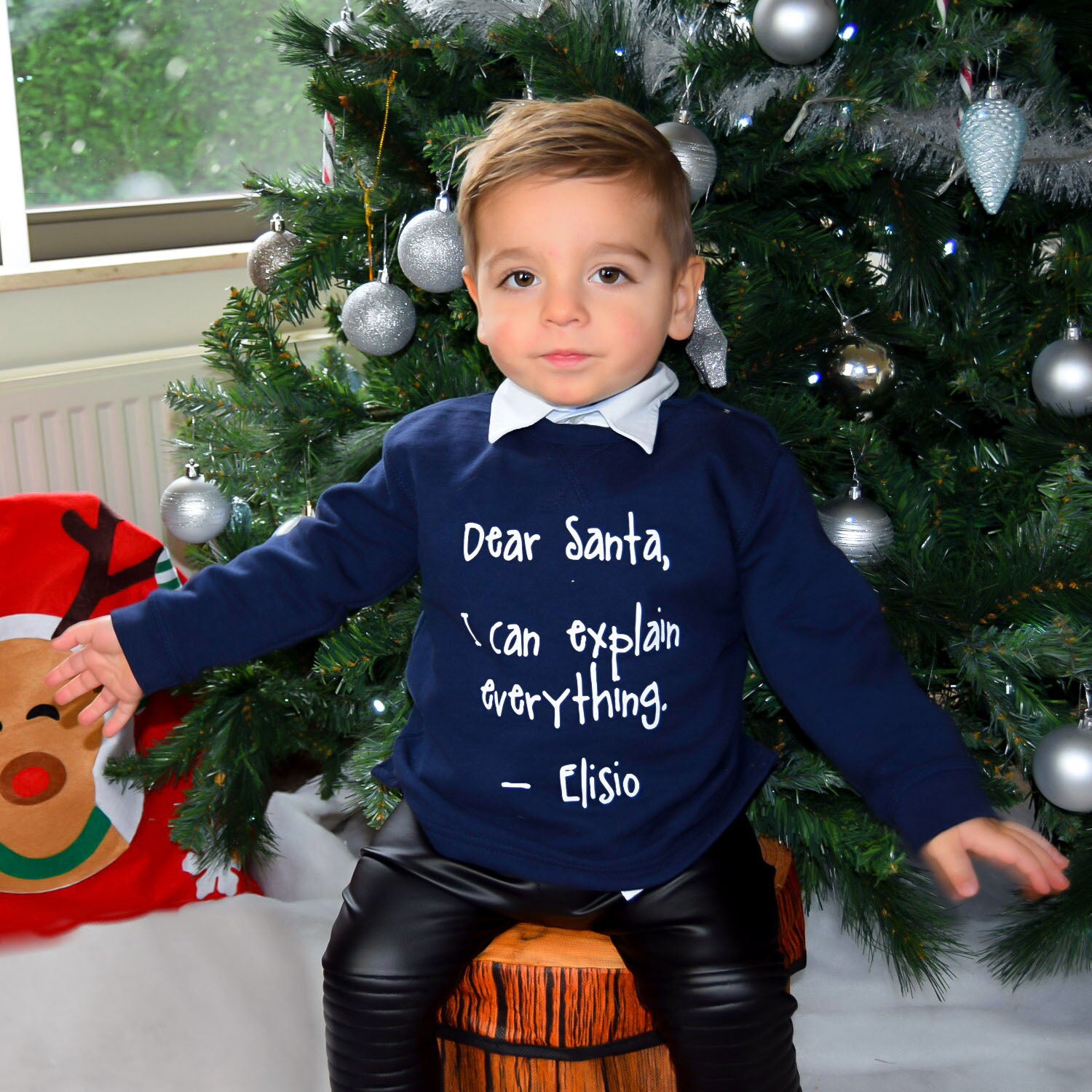Boy with Navy sweater with 'Santa, I can explain everything' print by KMLeon in front of christmas tree.
