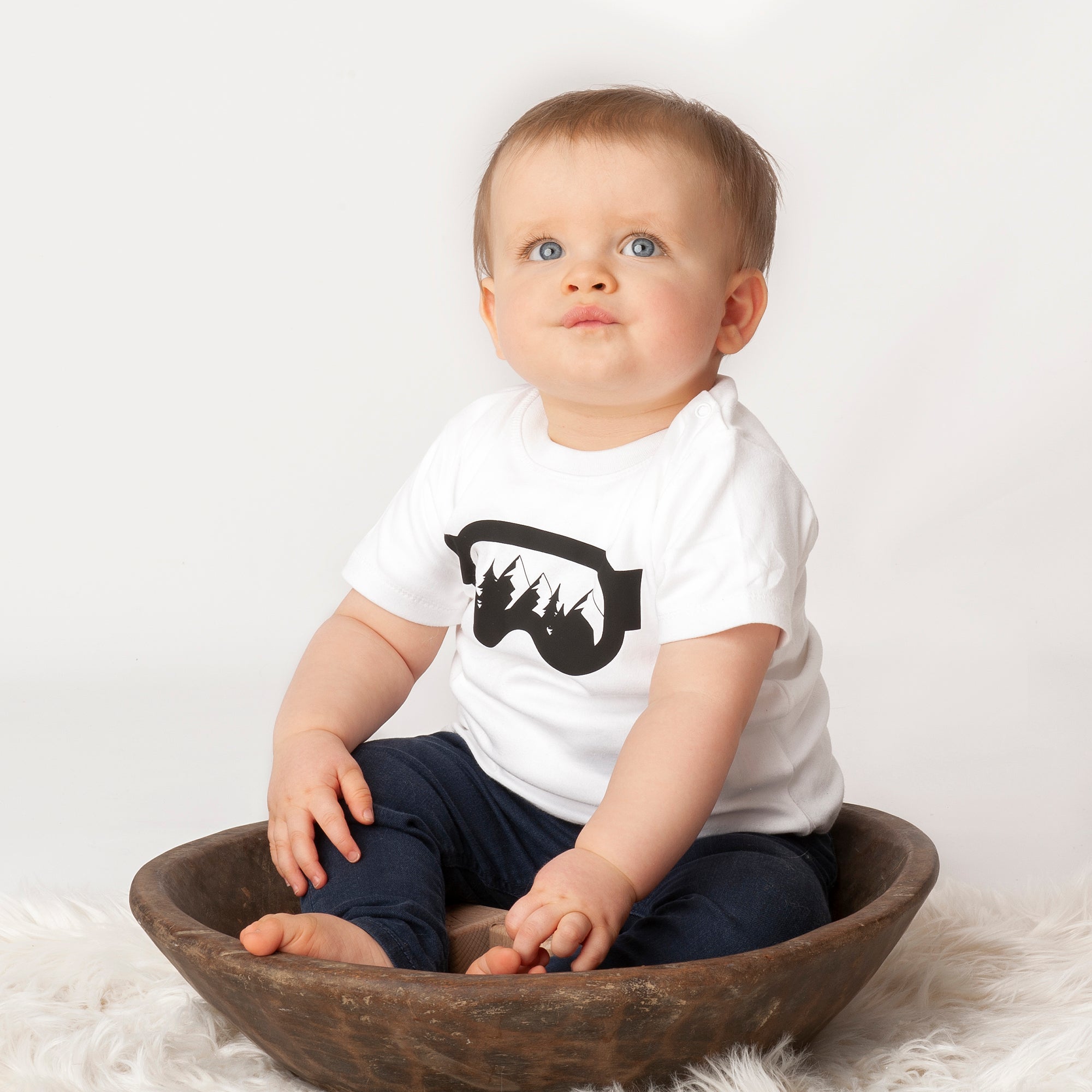 Little boy wearing white shirt with ski goggles print by KMLeon sitting in brown dish.