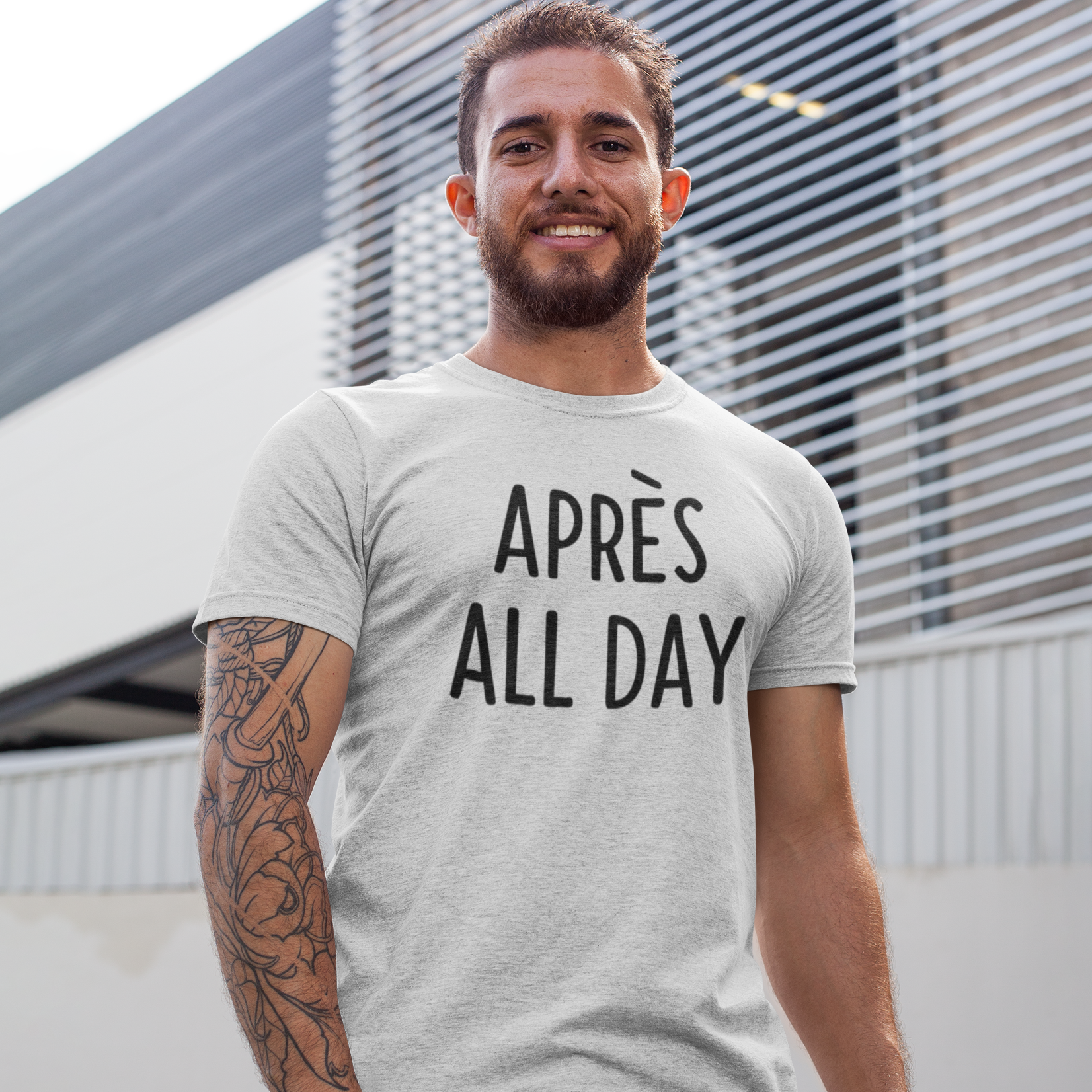 Man with beard and tattoo wearing heather grey shirt with 'Après all day' print by KMLeon.