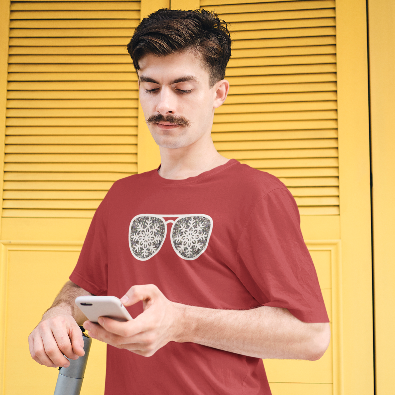 Man with mustache looking at his phone in front of yellow door, wearing red shirt with glitter snow star glasses by KMLeon.