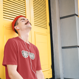 Man with mustache and red beanie listening to music with closed eyes, leaning against yellow door, wearing red shirt with glitter snow star glasses by KMLeon.