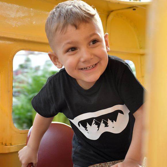 Young boy wearing black shirt with ski goggles print by KMLeon in yellow bus.