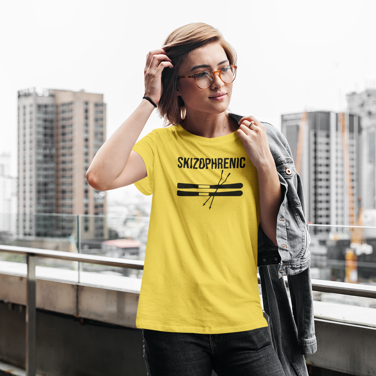 Woman with glasses in the city wearing yekllow shirt with 'Skizophrenic' print by KMLeon.