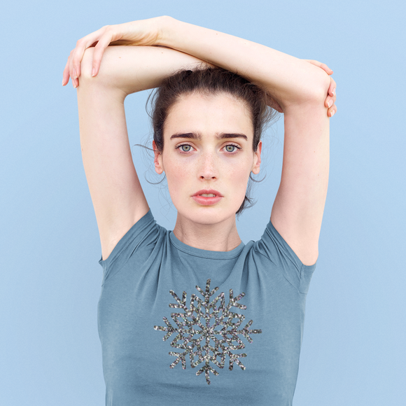 Woman wearing indigo shirt, with glitter snow star print by KMLeon, holding arms above head.