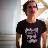 Man with mustache wearing black shirt with 'Staching through the snow' print by KMLeon, looking away from camera.