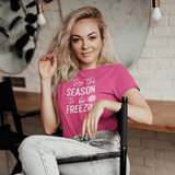 Blonde woman sitting on chair, wearing pink shirt with ''tis the season to be freezin'' print by KMLeon.